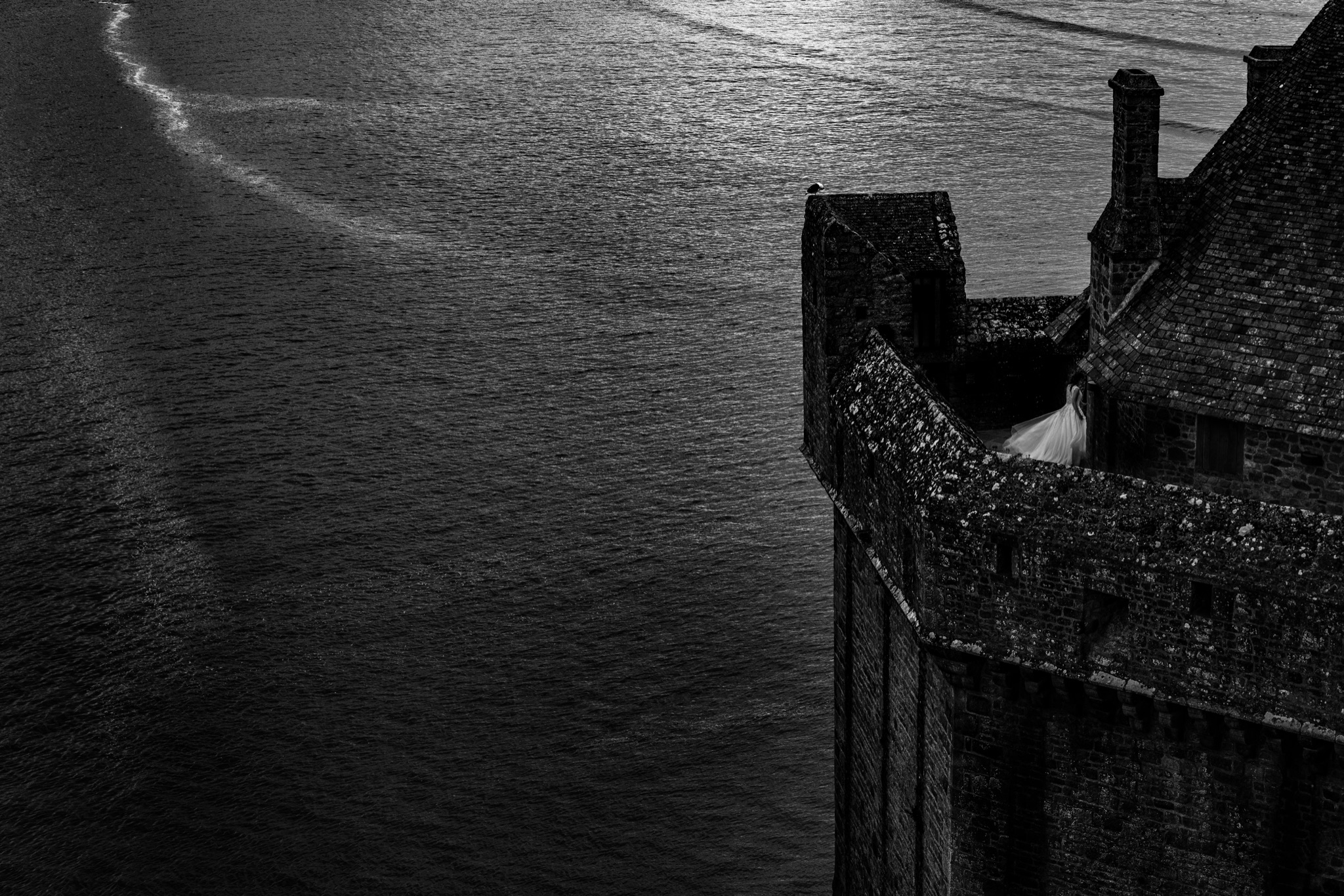 Looking down on a rampart tower of Mont-Saint-Michel surrounded by the sea, the bride tiny on the parapet walk — photograph awarded by the Fearless Awards — Arnaud Chapelle