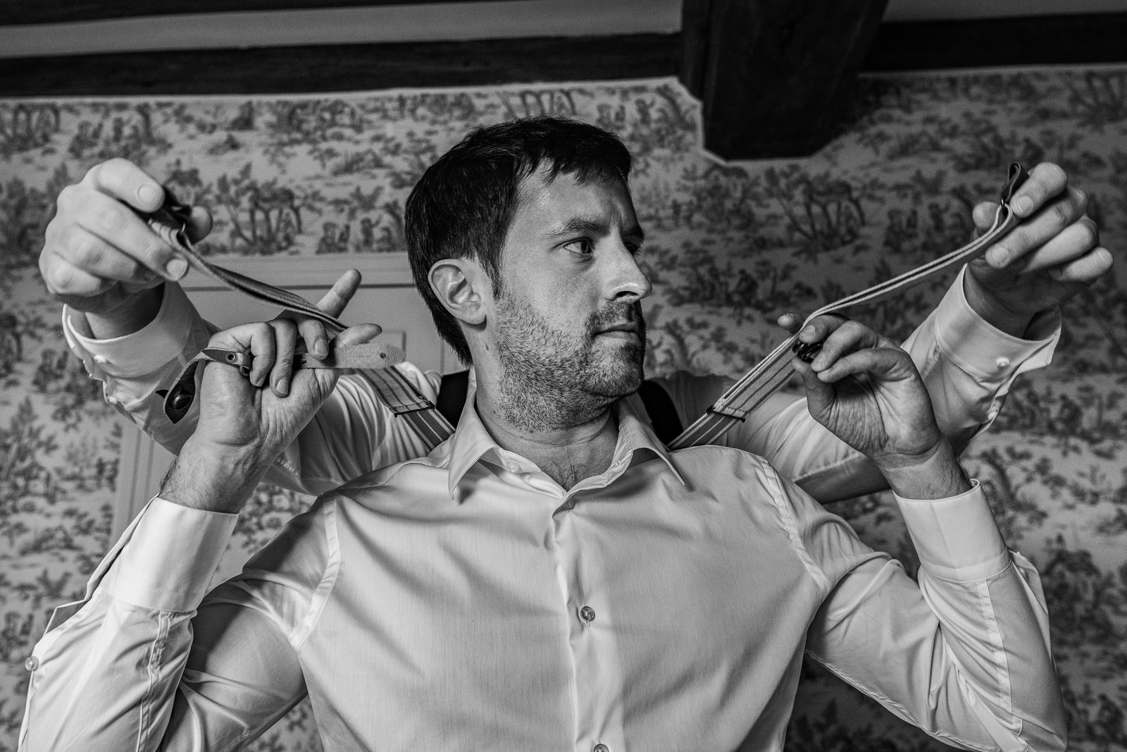 Benjamin règle ses bretelles, en noir et blanc — préparatifs du marié au Château de la Roque — Arnaud Chapelle