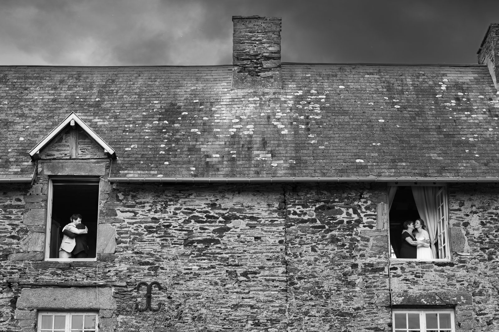 Deux fenêtres ouvertes sur la façade de schiste, la mariée et ses proches aux fenêtres — Château de la Roque, Théreval — Arnaud Chapelle