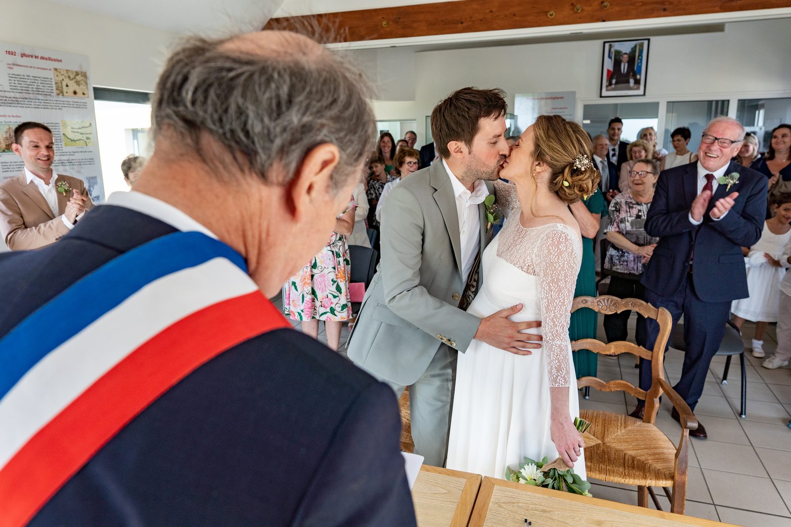Le maire en écharpe tricolore, les mariés s'embrassent devant une salle comble — mairie de Tourville-sur-Sienne — Arnaud Chapelle