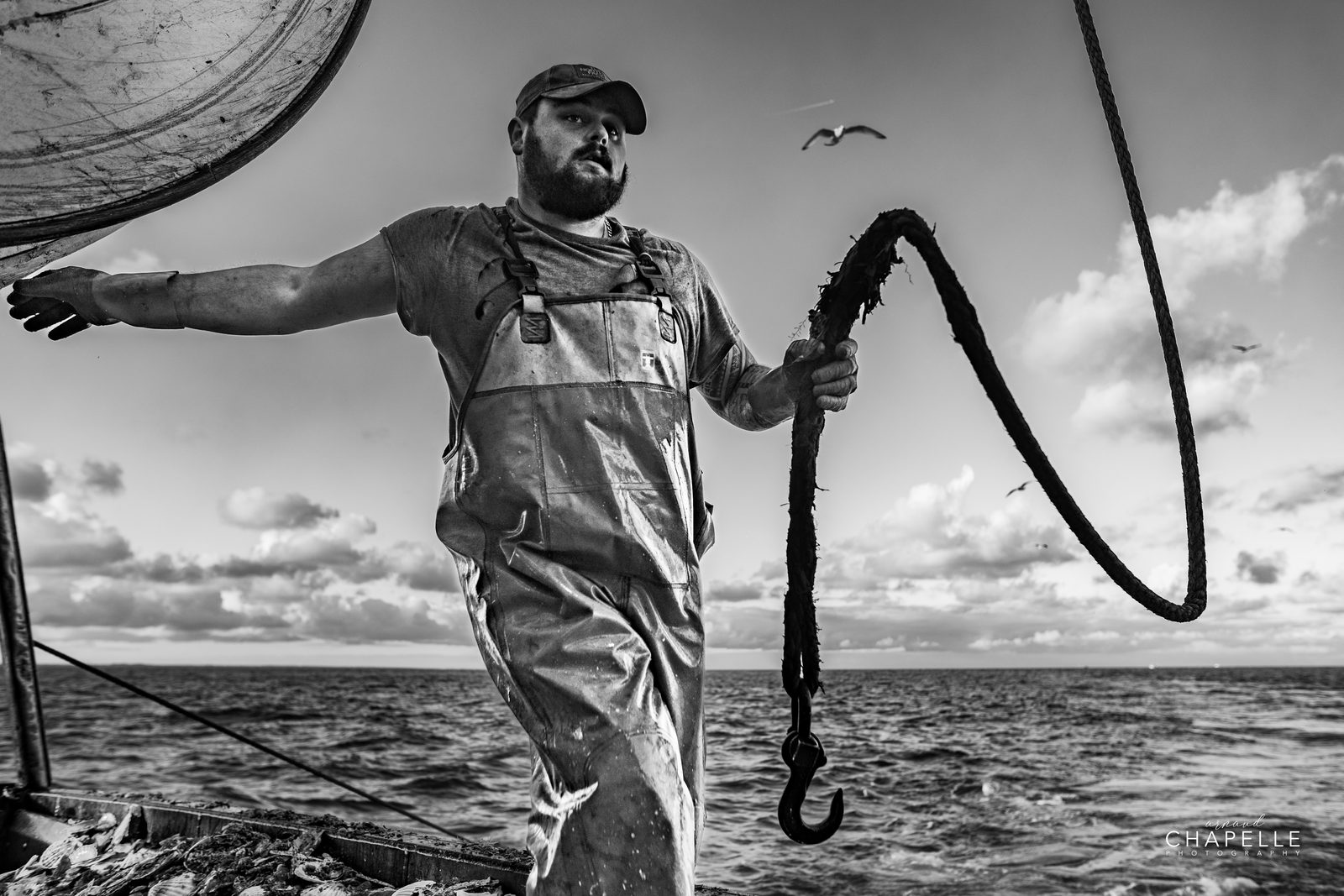 Un marin lance un cordage sur le pont, la mer derrière, en noir et blanc — Arnaud Chapelle