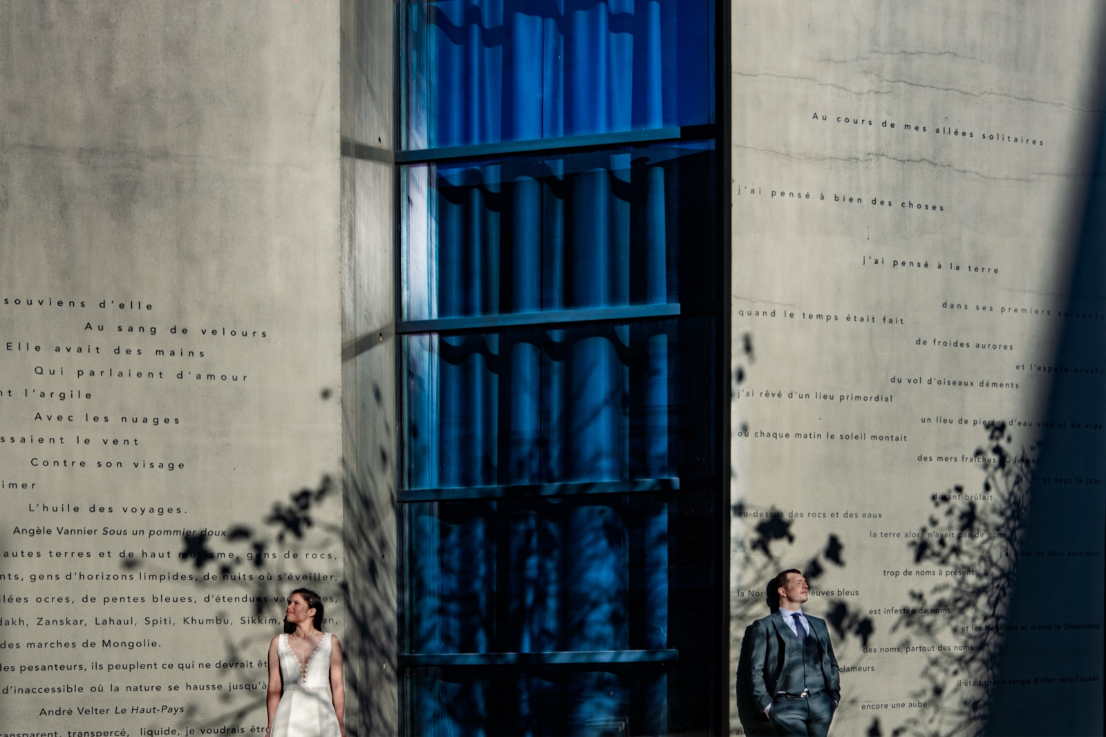 Marine et Alexandre de part et d'autre d'une grande verrière bleue, sur un mur couvert de textes — séance couple à Saint-Malo — Arnaud Chapelle