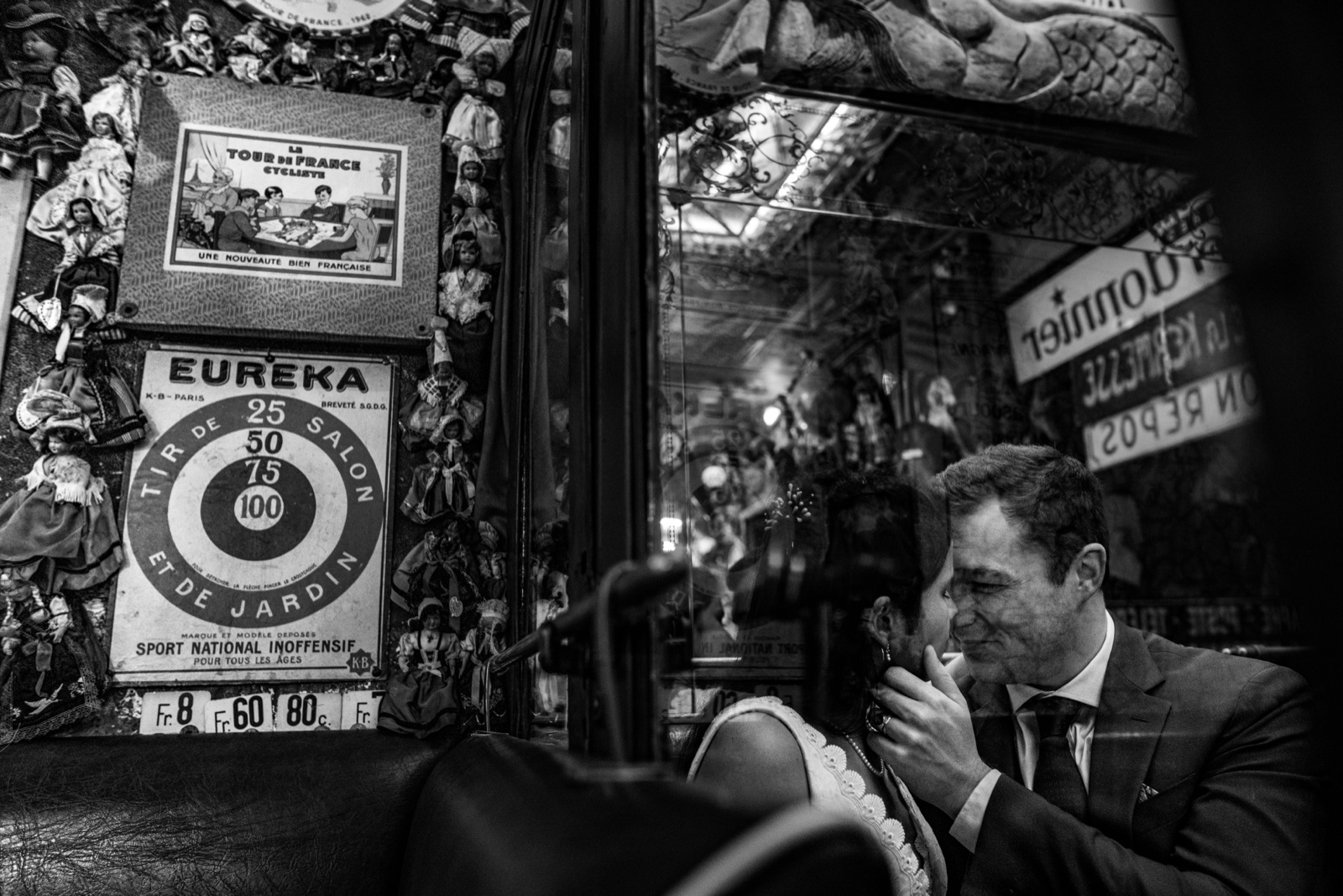 Alexandre embrasse la main de Marine, vus à travers la vitrine du café La Java, en noir et blanc — Saint-Malo — Arnaud Chapelle