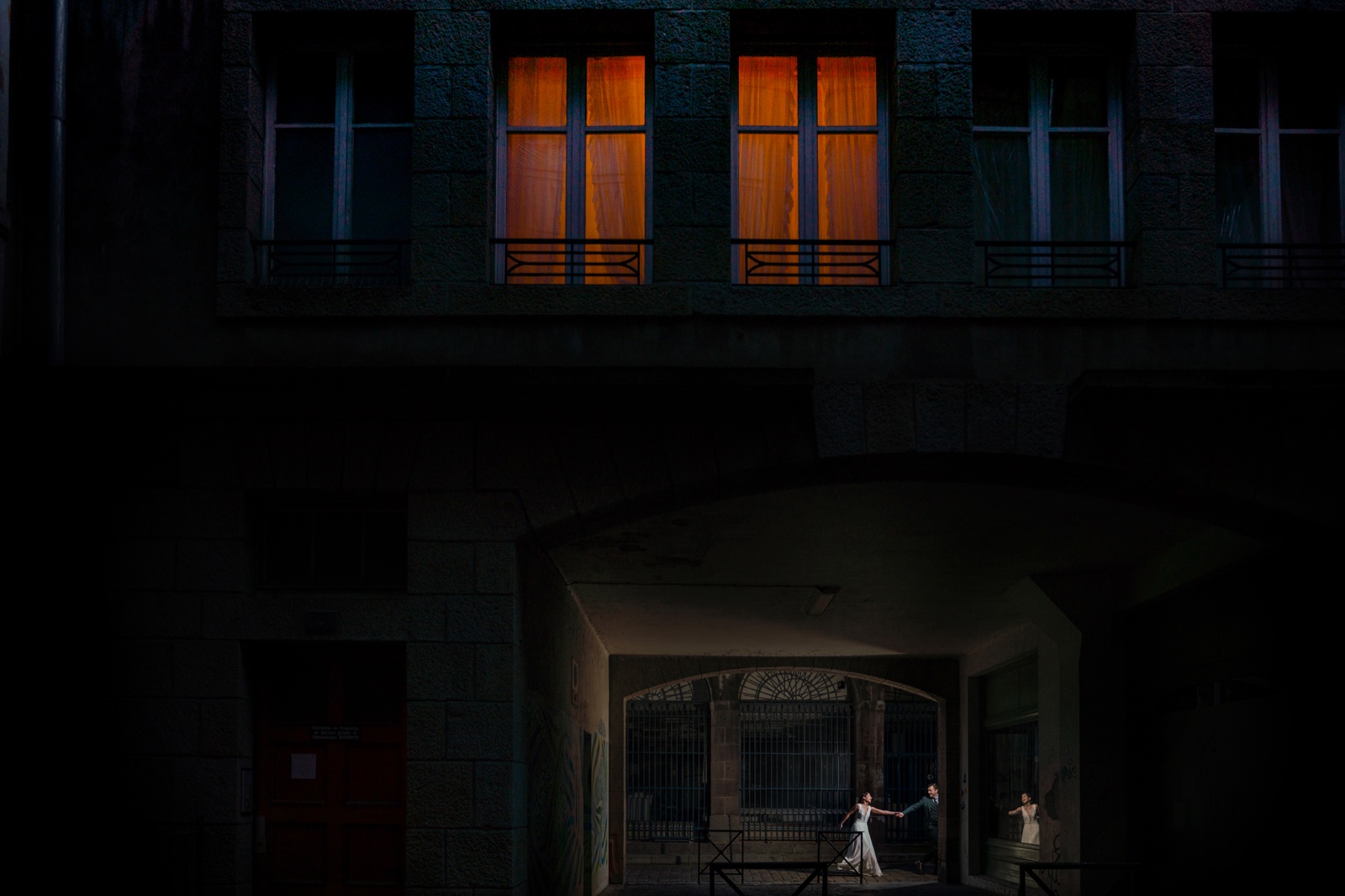 Le couple sous une arche de l'intra-muros la nuit, fenêtres éclairées à l'étage — séance couple à Saint-Malo — Arnaud Chapelle
