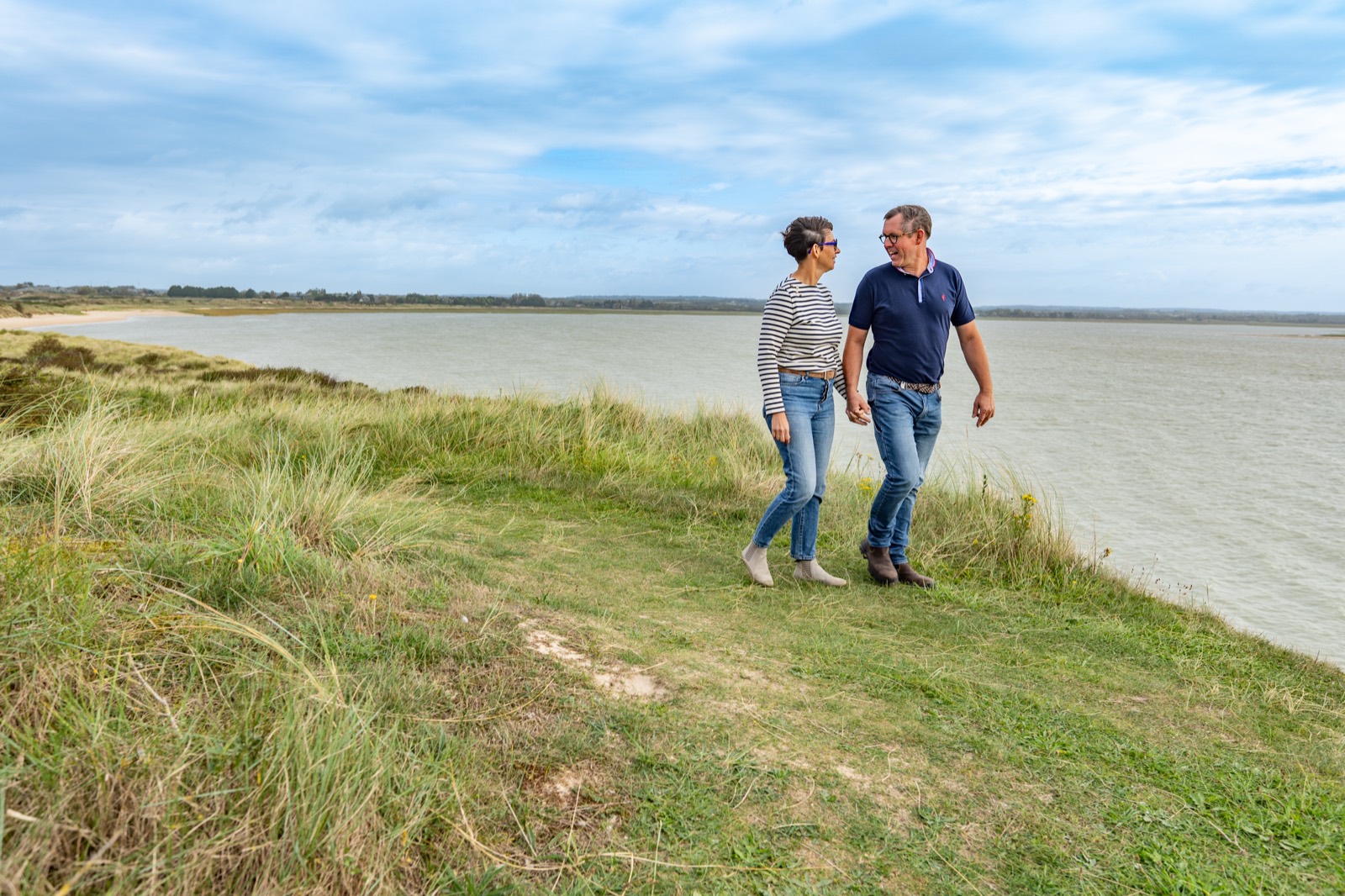 Fabrice et Véronique, dirigeants des Menuiseries du Cotentin, marchant dans les dunes face à la mer — portrait d'entreprise — Arnaud Chapelle