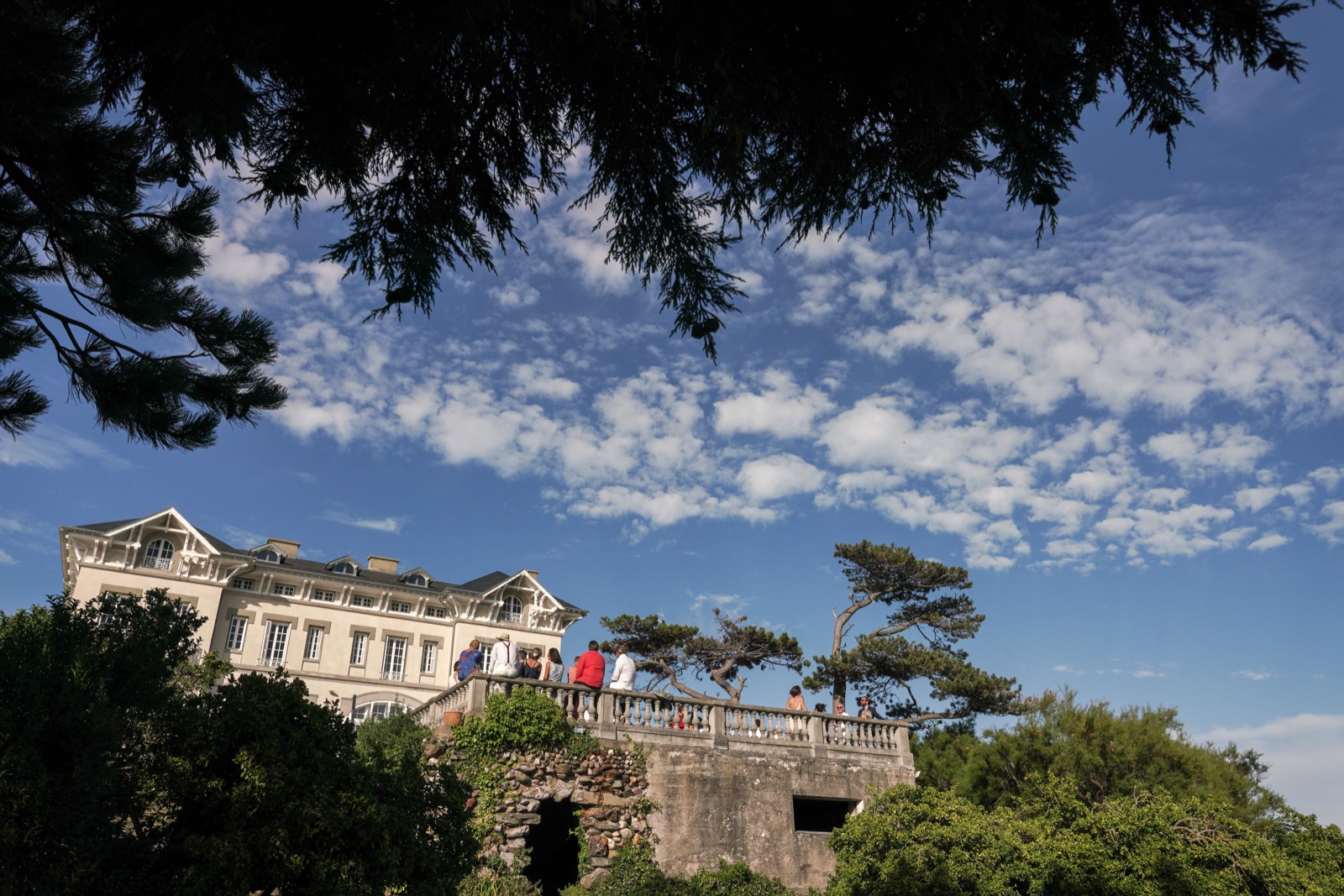 Le Château de la Crête vu d'en bas depuis le sentier, les invités accoudés à la balustrade — mariage à Granville (Manche) — Arnaud Chapelle
