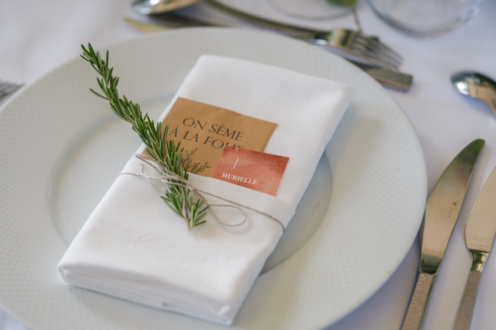 Marque-place en papier kraft « on sème à la folie » et branche de romarin nouée sur la serviette — dîner de mariage au Château de la Crête, Granville — Arnaud Chapelle