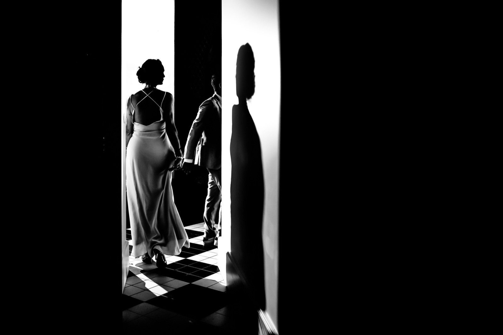 Silhouettes des mariés main dans la main dans un couloir à contre-jour, en noir et blanc — séance couple after-wedding, Granville — Arnaud Chapelle