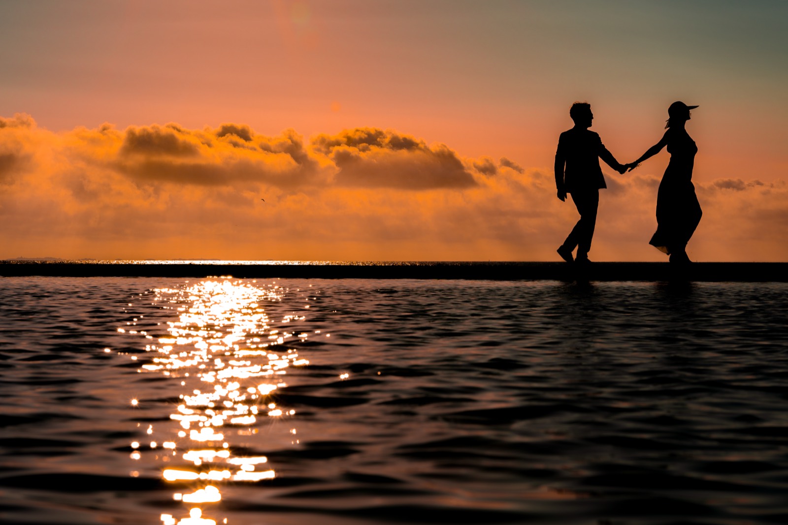 Le couple en silhouette sur la digue de Granville au coucher du soleil, la mer devant eux — séance after-wedding — Arnaud Chapelle photographe Normandie