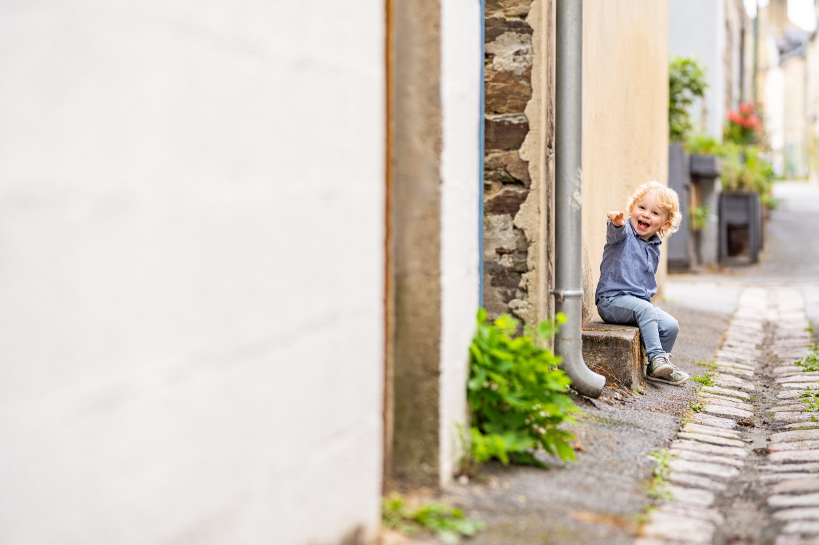 Le petit garçon assis sur une marche au coin d'une ruelle, grand sourire — séance famille à Cancale — Arnaud Chapelle