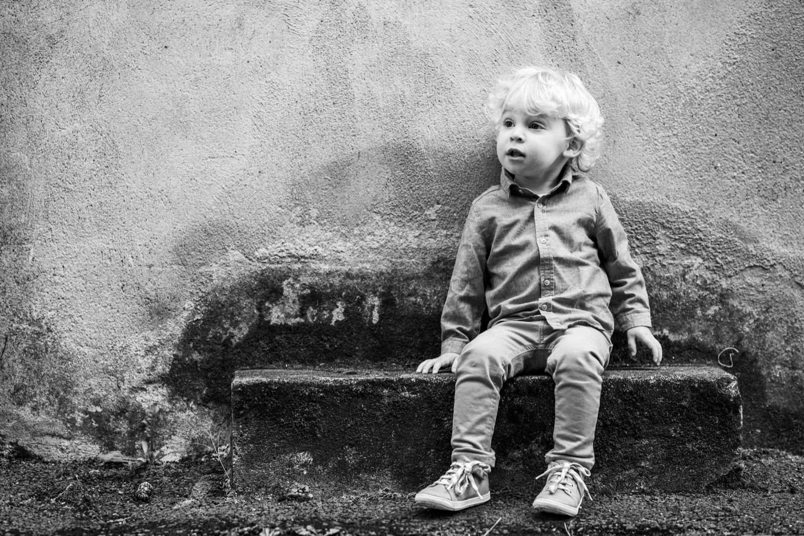 Le petit garçon assis sur un banc de pierre, l'air rêveur, en noir et blanc — séance famille à Cancale — Arnaud Chapelle