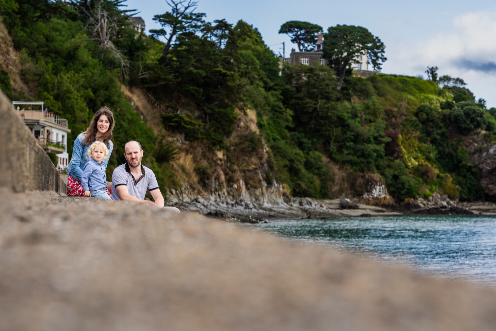 La famille assise sur la digue d'une crique de Cancale, les falaises vertes derrière — Arnaud Chapelle