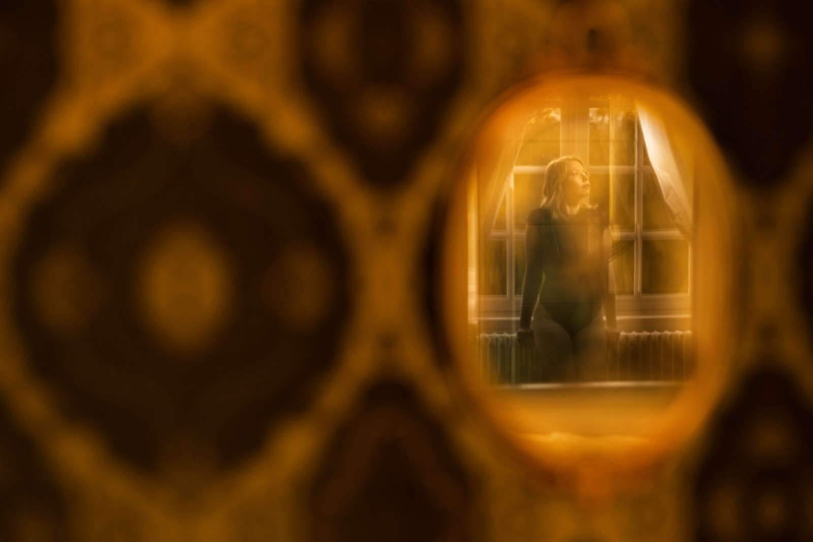 Reflet dans un petit miroir ovale : une silhouette à la fenêtre, au fond de la pièce — séance boudoir près de Bayeux (Calvados) — Arnaud Chapelle