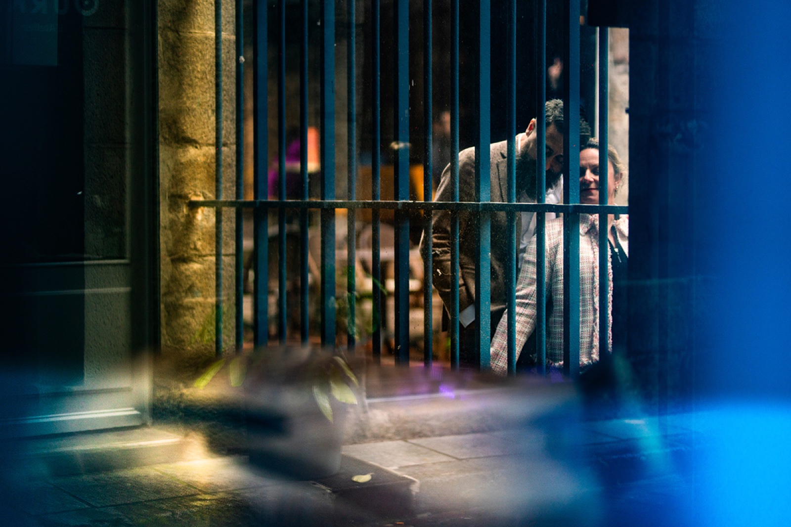 Le couple aperçu à travers une grille, dans les reflets du soir — séance engagement à Saint-Malo — Arnaud Chapelle