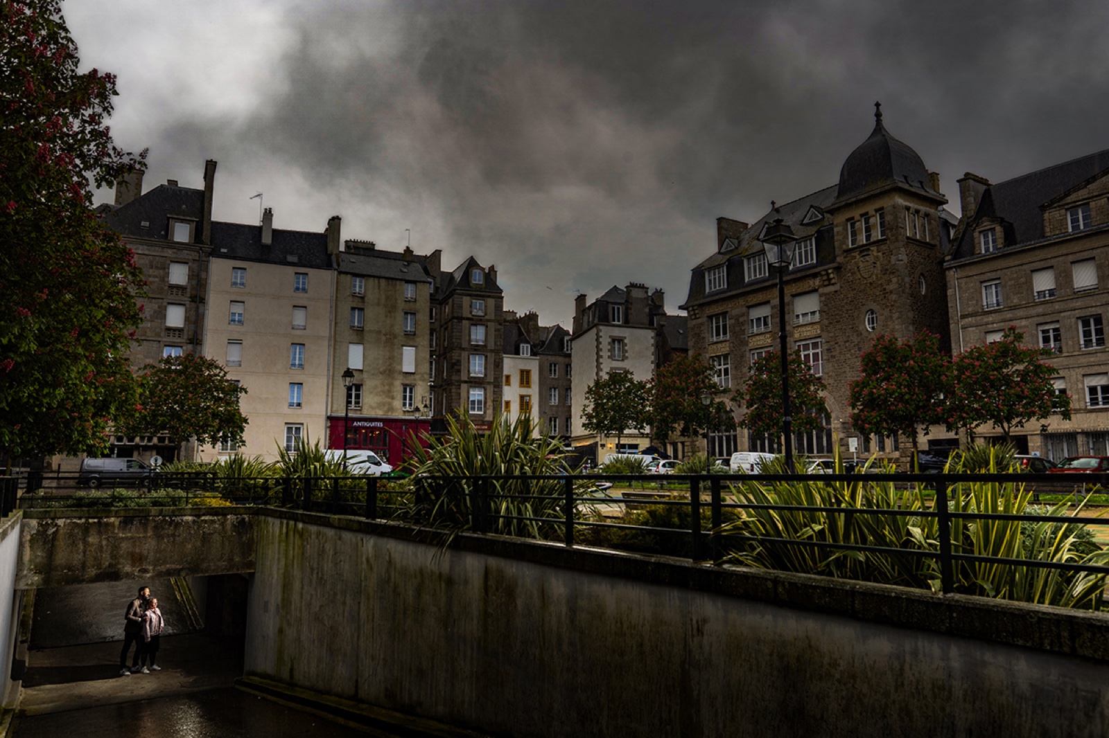 Les toits et façades de Saint-Malo sous un ciel spectaculaire, le couple en contrebas — séance engagement — Arnaud Chapelle