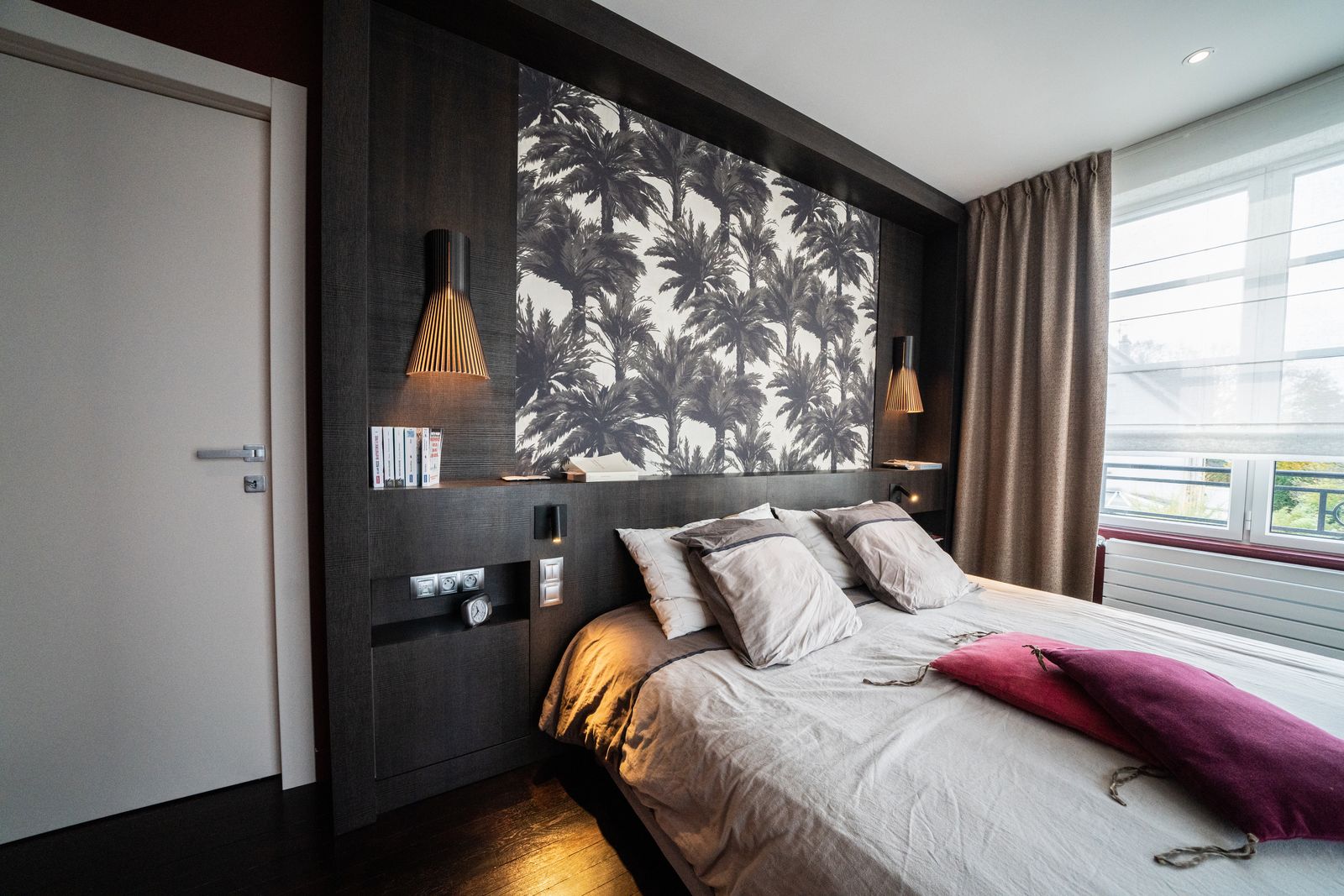 Dark bedroom, palm-print wallpaper and wooden headboard