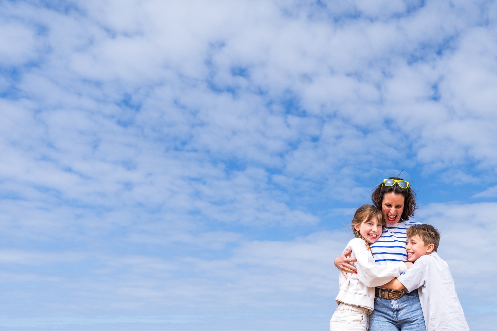 A mother and her two children laughing together under a wide Normandy sky at Omaha Beach