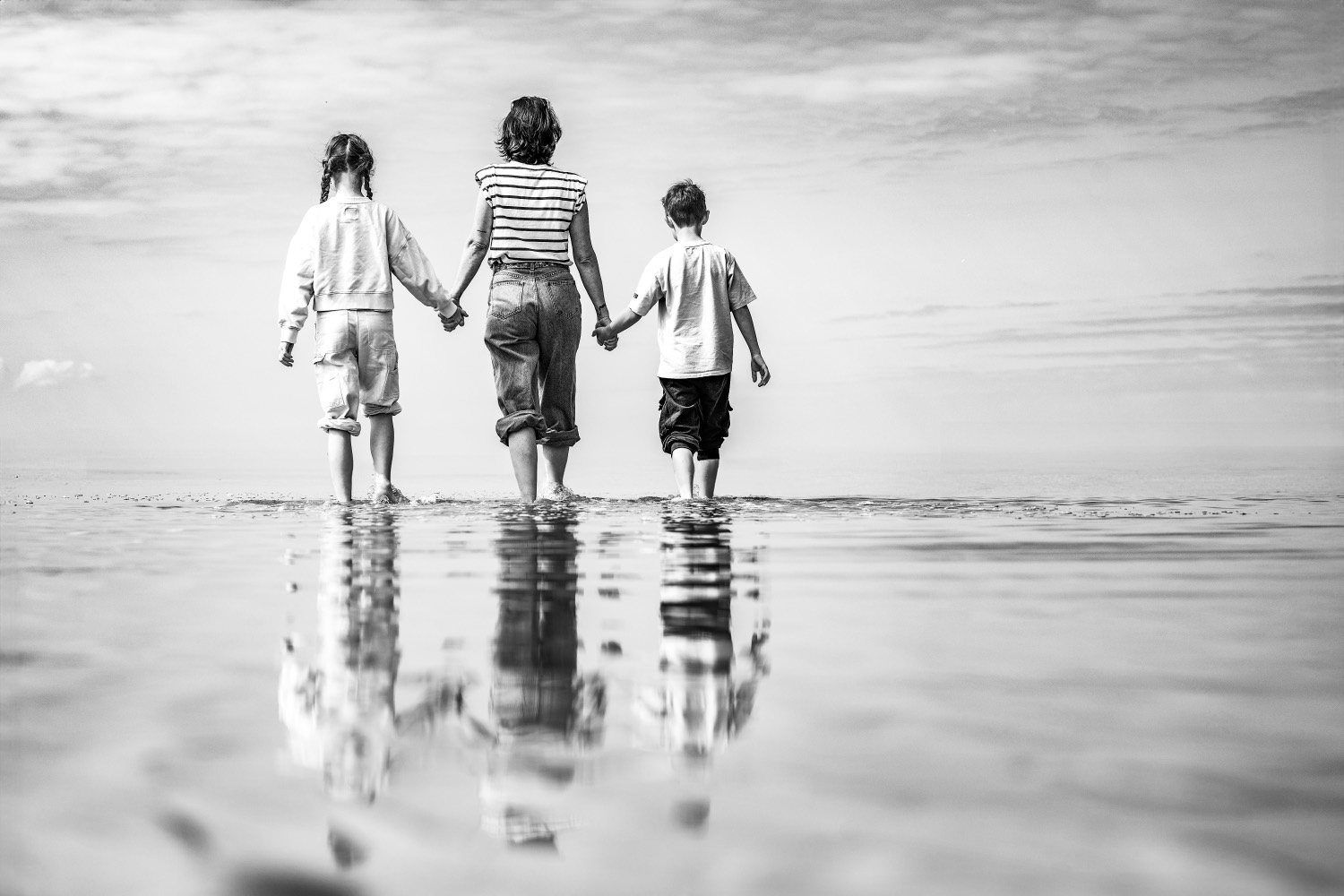 Black and white photograph of a mother and her two children walking hand in hand into the sea in Normandy
