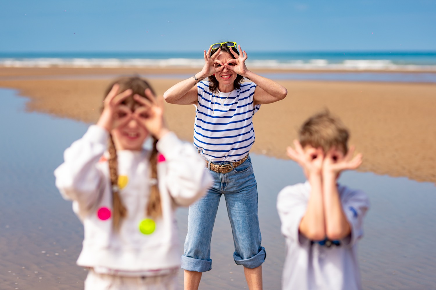 A family making binocular shapes with their hands on the wide sands of Omaha Beach
