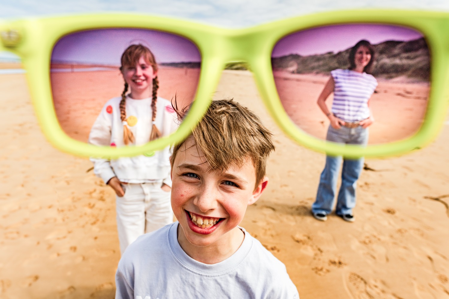 A laughing boy seen through a giant pair of sunglasses, his mother and sister framed in the lenses