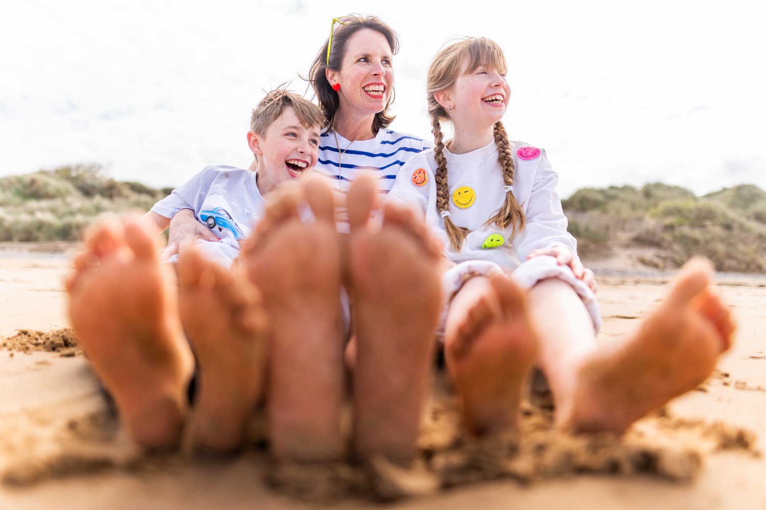 A mother and her two children sitting on the sand at Omaha Beach, bare feet in the foreground