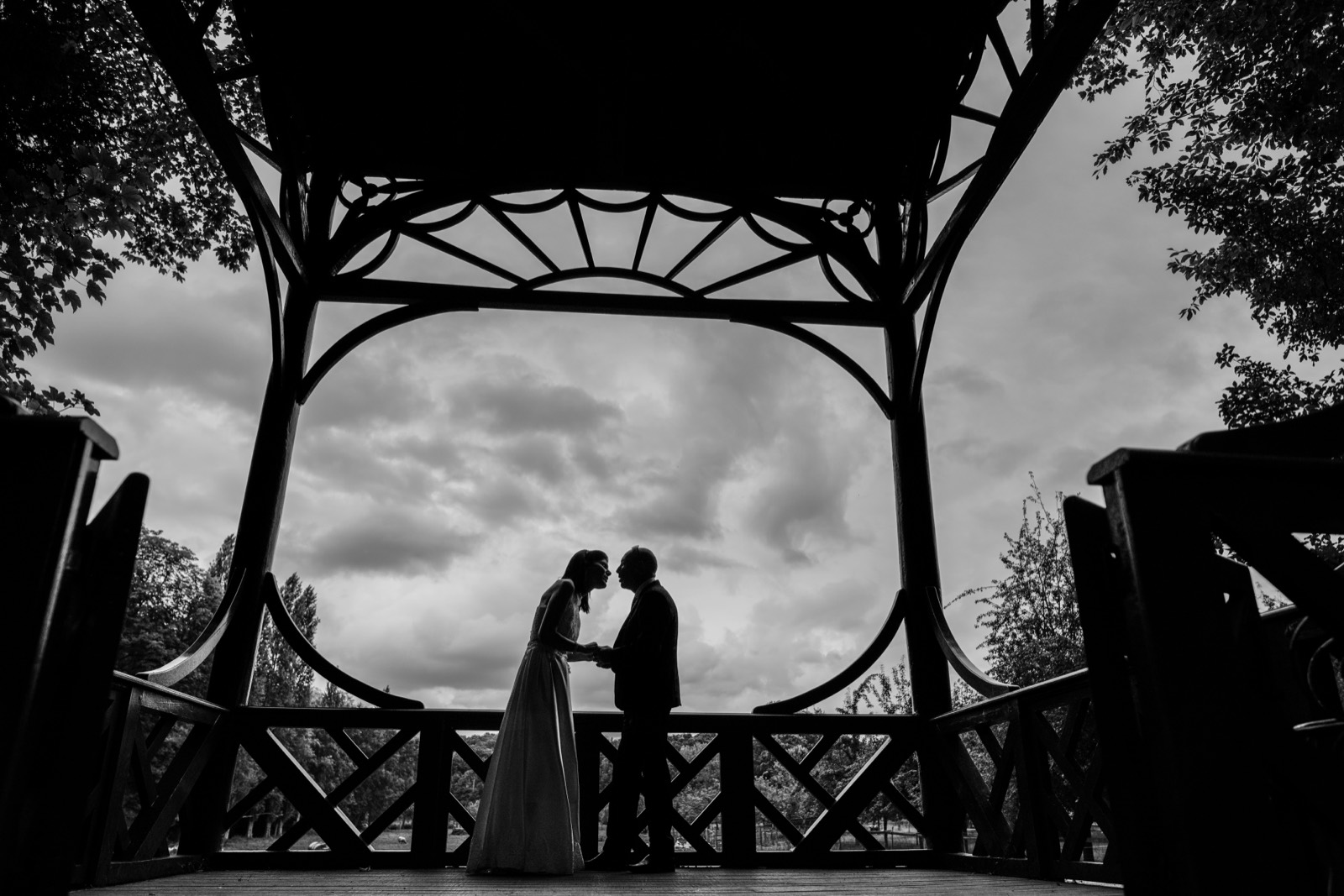 Silhouette des mariés sous une fabrique du parc, ciel dramatique en noir et blanc — Château de Canon, Mézidon — Arnaud Chapelle