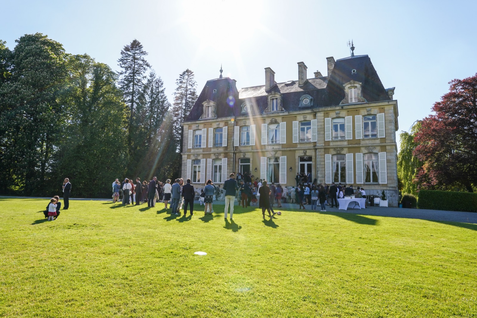 Le Château du Perron et sa façade, les invités sur la pelouse au soleil — lieu de mariage à Saint-Aubin-du-Perron (Manche) — Arnaud Chapelle