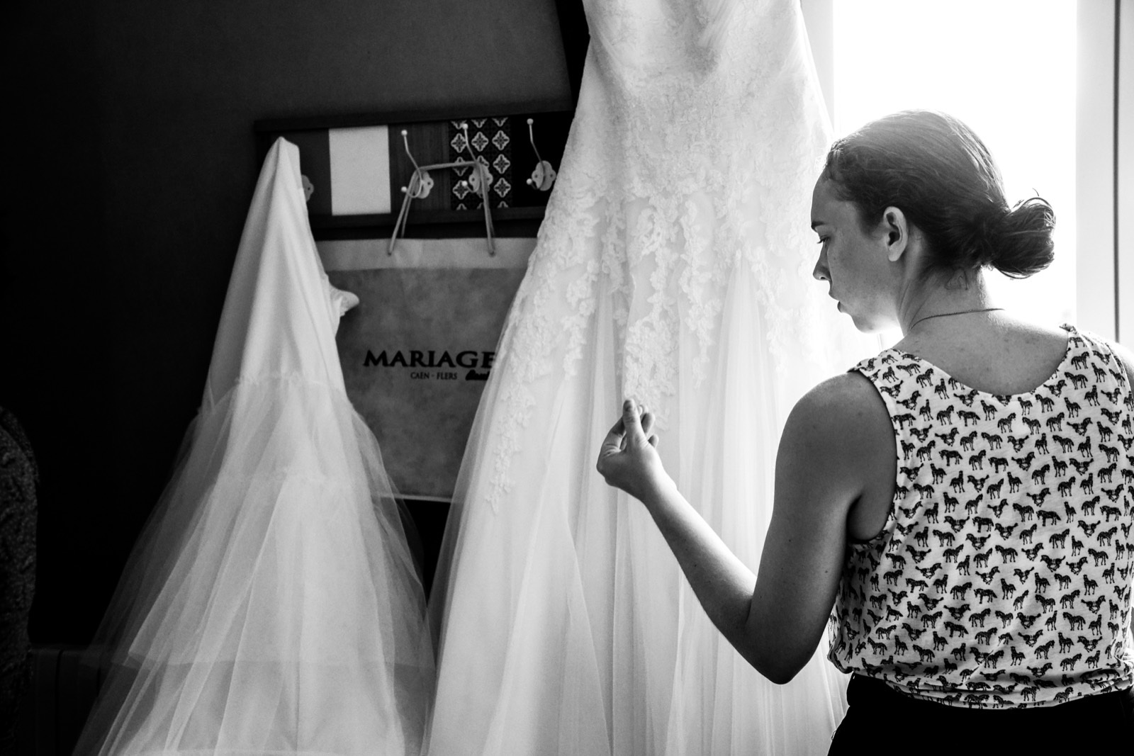 La robe de mariée suspendue, une amie l'admire, en noir et blanc — préparatifs au Domaine de Cauvicourt (Calvados) — Arnaud Chapelle