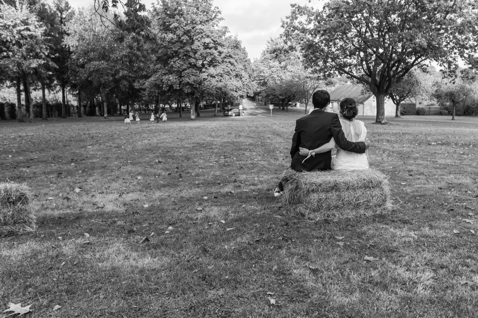 Les mariés assis sur une botte de paille face au parc, en noir et blanc — mariage au Domaine de Pont-Ramond (Orne) — Arnaud Chapelle