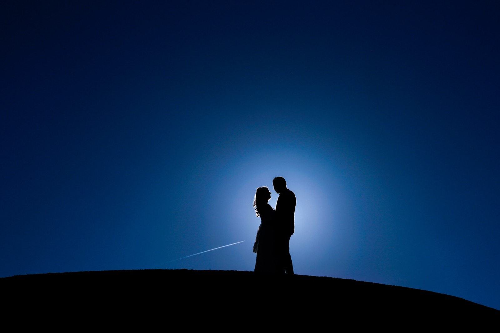 Les mariés en silhouette sur une colline, ciel bleu nuit — portrait au Domaine du Grand Caugy, près de Bayeux (Calvados) — Arnaud Chapelle