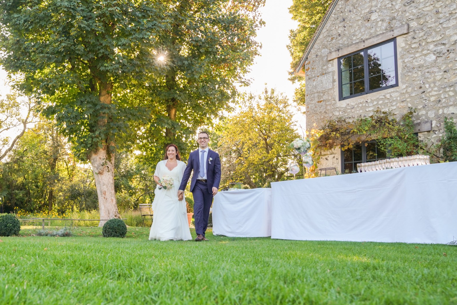 Les mariés dans le jardin devant la grange en pierre — lieu de mariage à La Dîme de Giverny (Eure) — Arnaud Chapelle