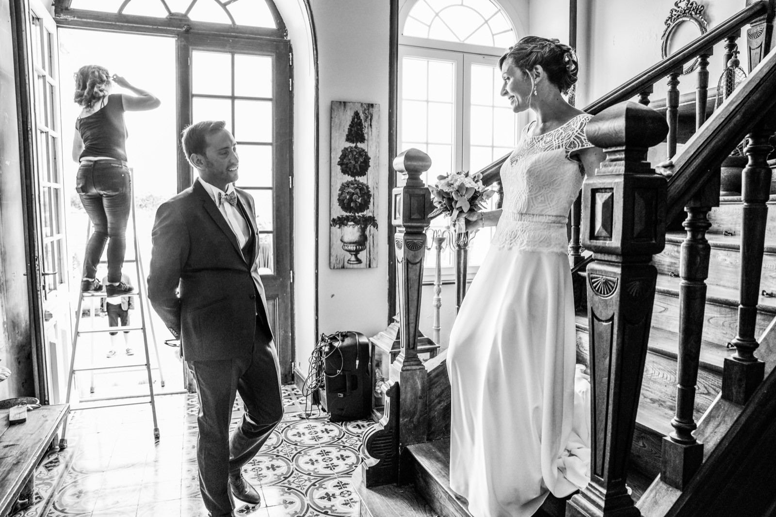La mariée dans l'escalier du manoir, le marié la découvre, en noir et blanc — mariage au Manoir de Chivré (Calvados) — Arnaud Chapelle