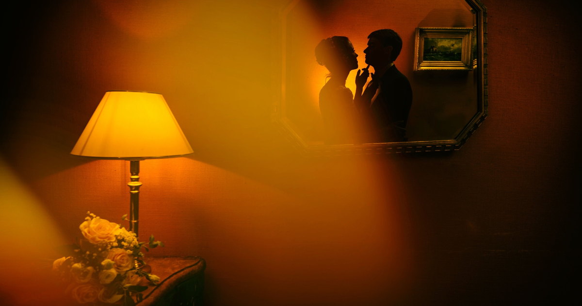 Wedding story: the couple reflected in a mirror, by lamplight — Arnaud Chapelle